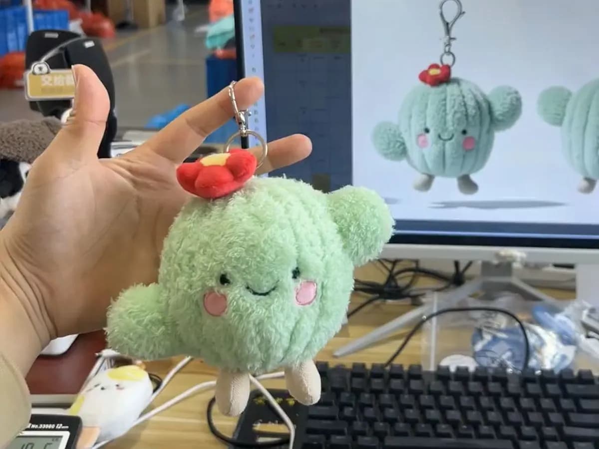 Cactus plush charm held in front of the artwork it was drawn from