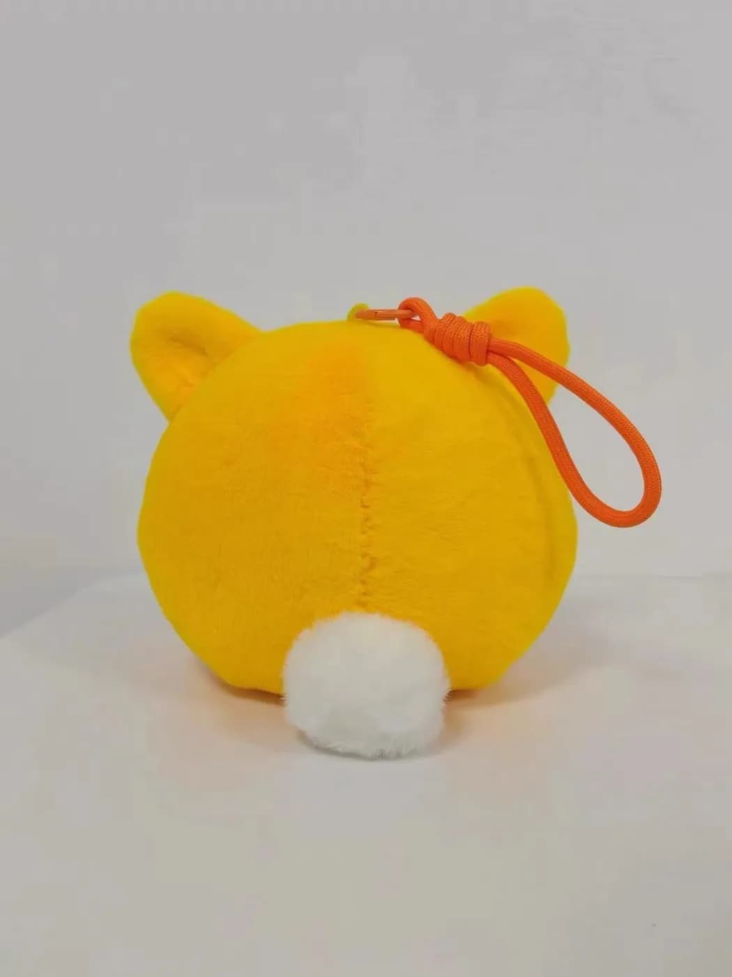 Yellow cat plush charm with a pompom tail and an elastic loop