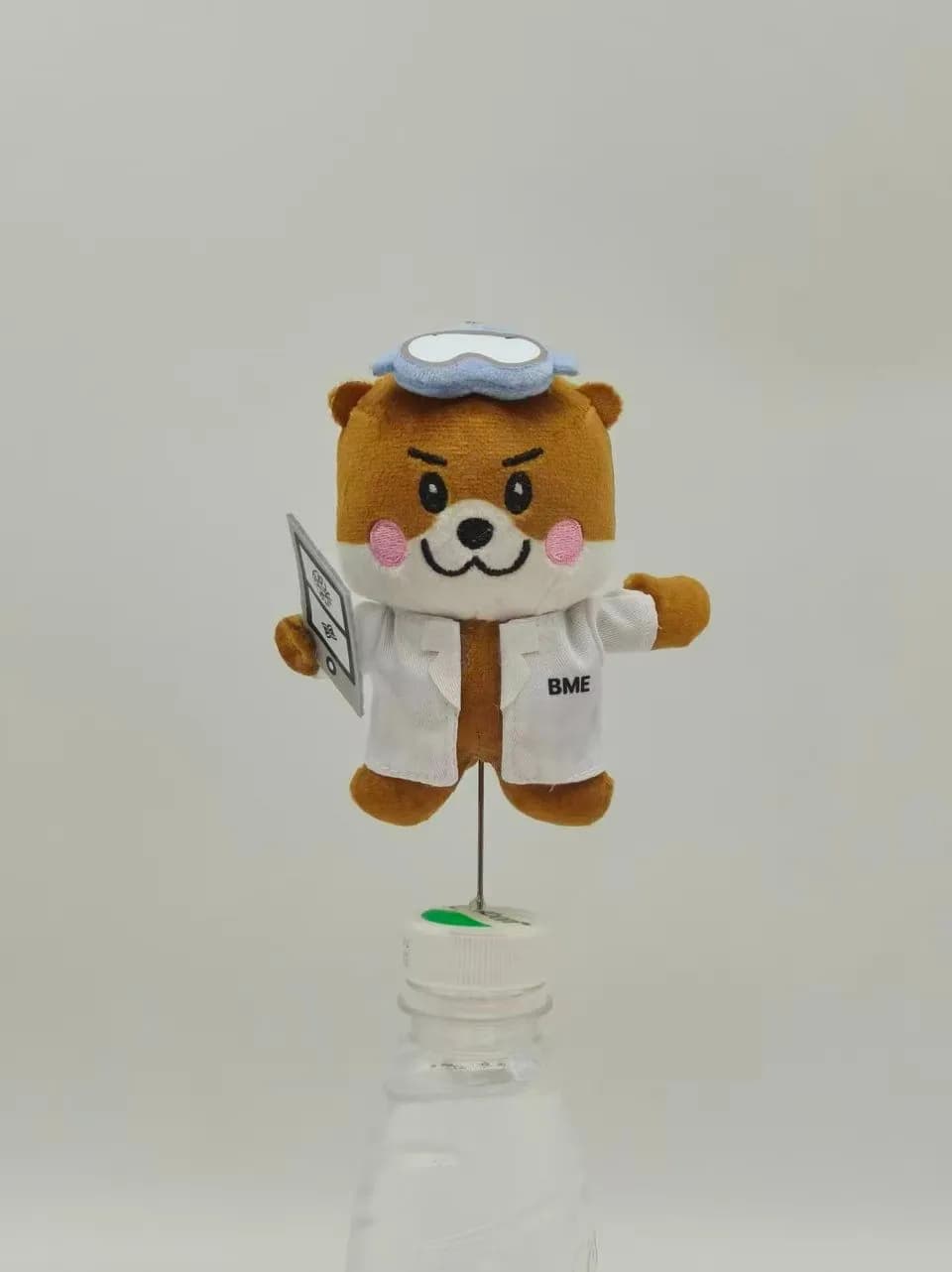 Bear mascot plush in a printed lab coat holding a clipboard