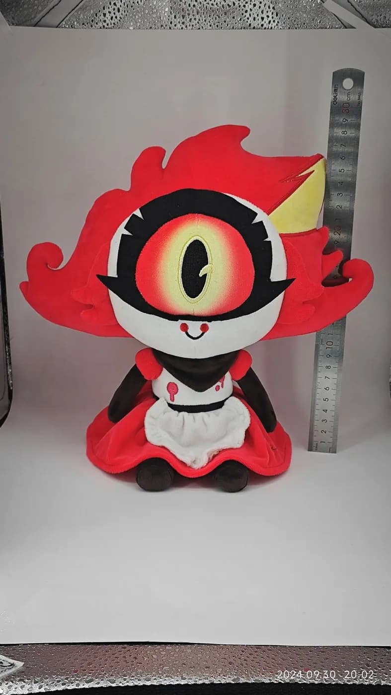 One-eyed character plush in a printed dress, measured against a steel rule
